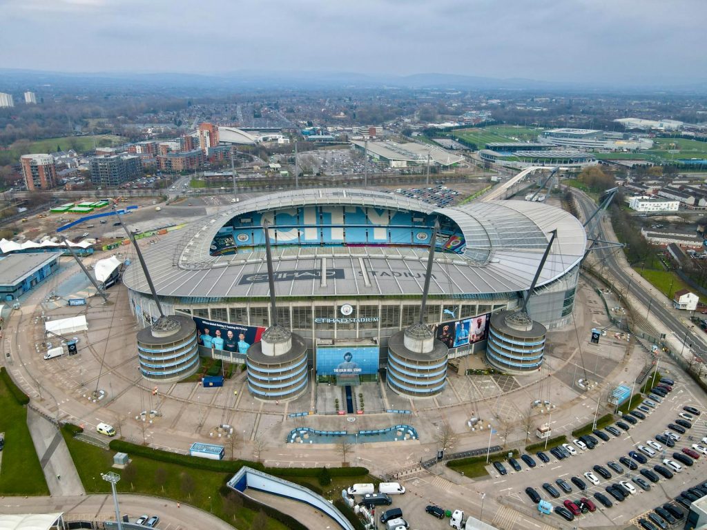 High-angle view of the iconic Etihad Stadium in Manchester, England, showcasing its modern architecture and surrounding cityscape.